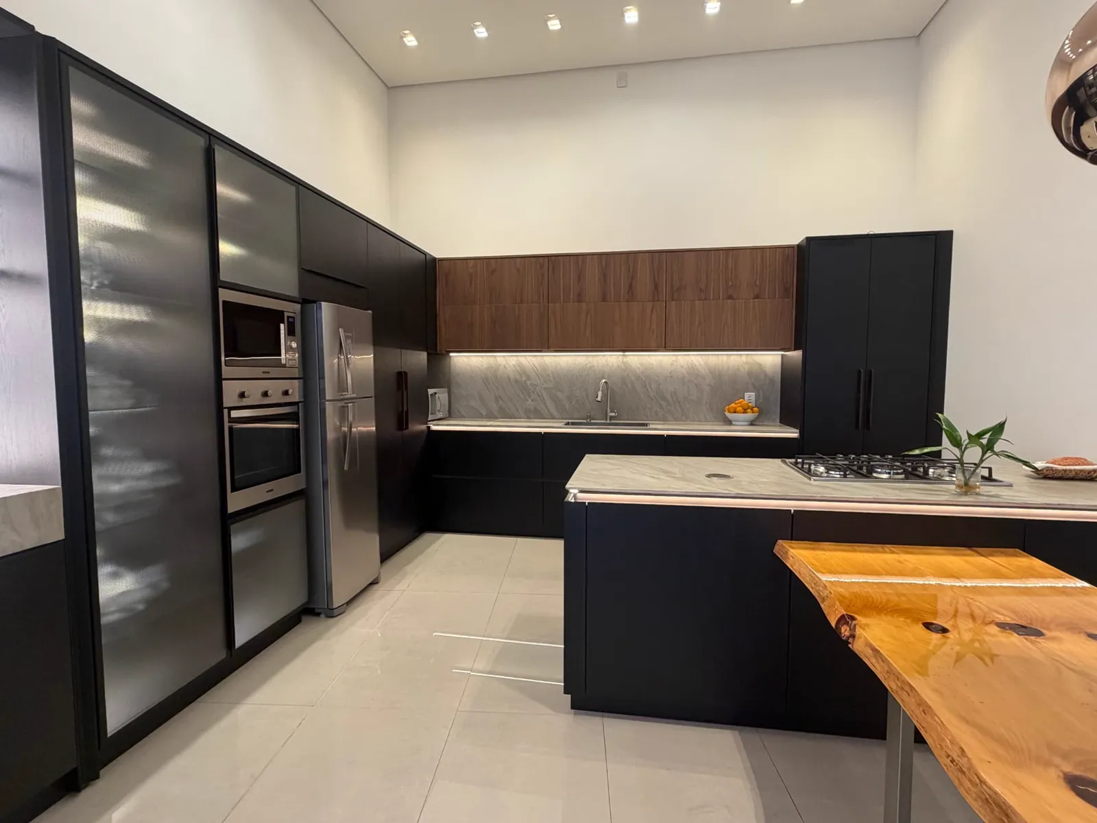 Cozinha preta planejada com ilha, cooktop e armários superiores em madeira