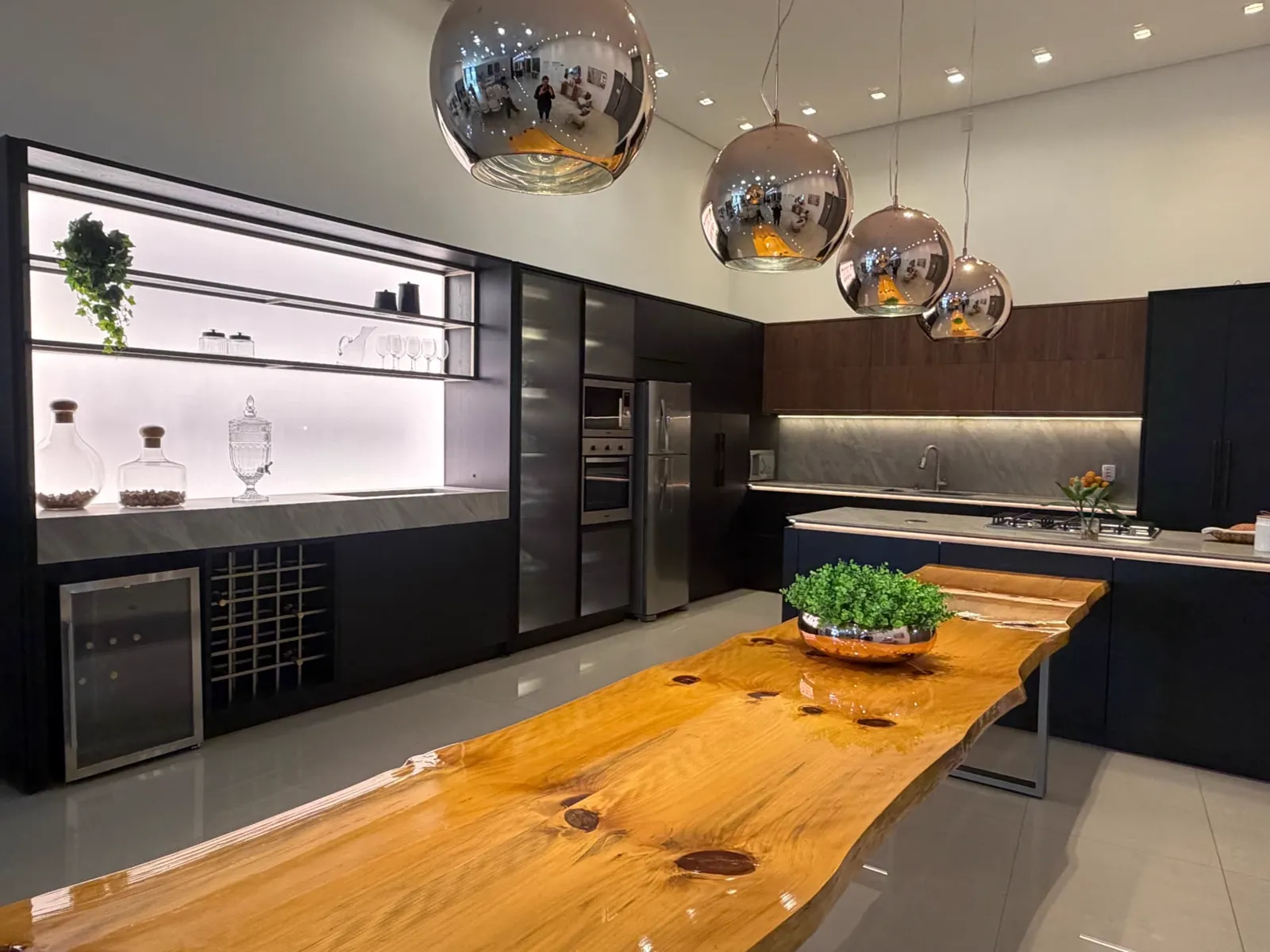 Cozinha gourmet do showroom em preto com mesa de tronco maciço e pendentes espelhados