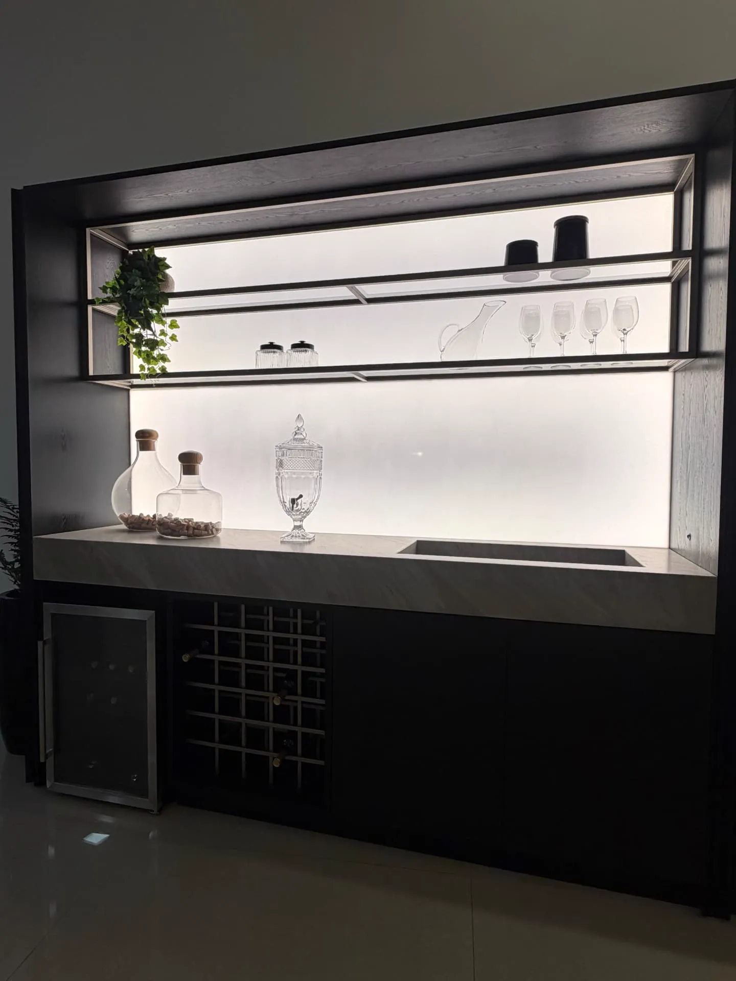 Bar planejado em preto com prateleiras de vidro iluminadas, adega e bancada em pedra