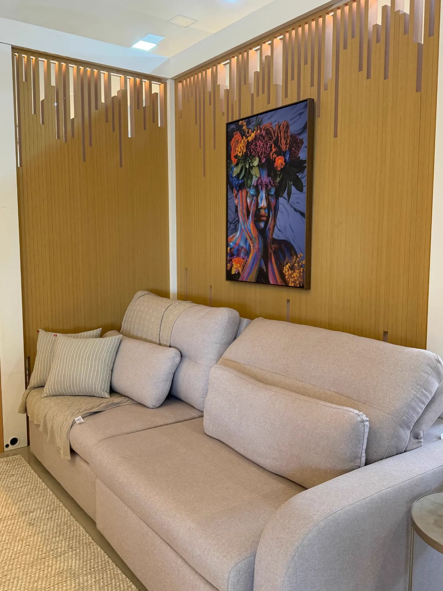 Estar do showroom com sofá bege e painel ripado em madeira com iluminação embutida